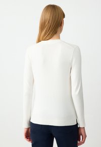Maglione bianco lavorato a maglia con maniche lunghe, scollo rotondo e orlo a coste. Tessuto liscio, design aderente, dettagli di cucitura visibili.
