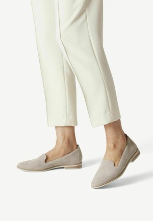 Zapatos de ante beige sin cordones con un diseño estriado, tacón bajo y un acento de madera clara en la suela. Combinados con pantalones crema ajustados.