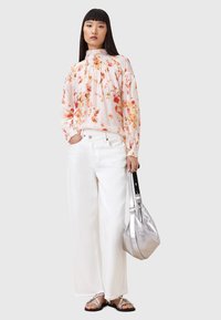 Bloes in zachte roze met oranje en rode bloemen, witte wijde jeans, zilveren handtas en platte sandalen. Lichte, luchtige stofstructuur.