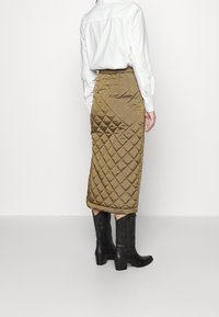 Quilted olivgrüne Midi-Rock mit Diamantmuster, kombiniert mit hohen schwarzen Cowboy-Stiefeln. Glatte Textur und gerades Silhouette.