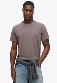 Grå bomulds t-shirt med rund halsudskæring og korte ærmer, båret med lys blå jeans og en grå sweater bundet om livet.