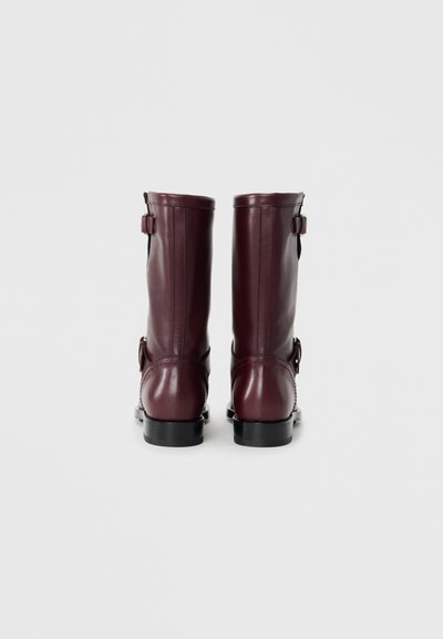 Burgundy leather boots with a glossy finish, mid-calf height, zipper and buckle accents, and a black rubber sole.