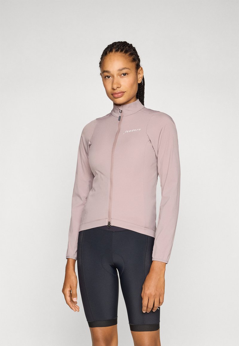Veste de cyclisme rose clair avec col montant et fermeture éclair intégrale, fabriquée en tissu extensible, associée à un short de cyclisme noir avec une large ceinture.