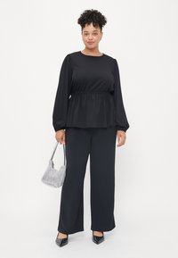 Black peplum top with long sleeves, paired with wide-leg black trousers. Silver houndstooth handbag and studded black heels.