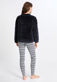 En marinblå fuskpälsjacka med ett texturerat mönster, i kombination med figurnära vita leggings med ett mörkblått nordiskt mönster.