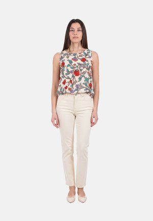 Donna che indossa un top floreale senza maniche con motivi rossi, viola e verdi, pantaloni crema a vita alta e ballerine crema, in piedi di fronte.