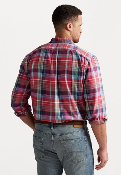 Sarkans un zils kostīms ar garām piedurknēm, ar pogu apkakli un sarullētām piedurknēm, valkāts virs gaiši ziliem džinsiem.