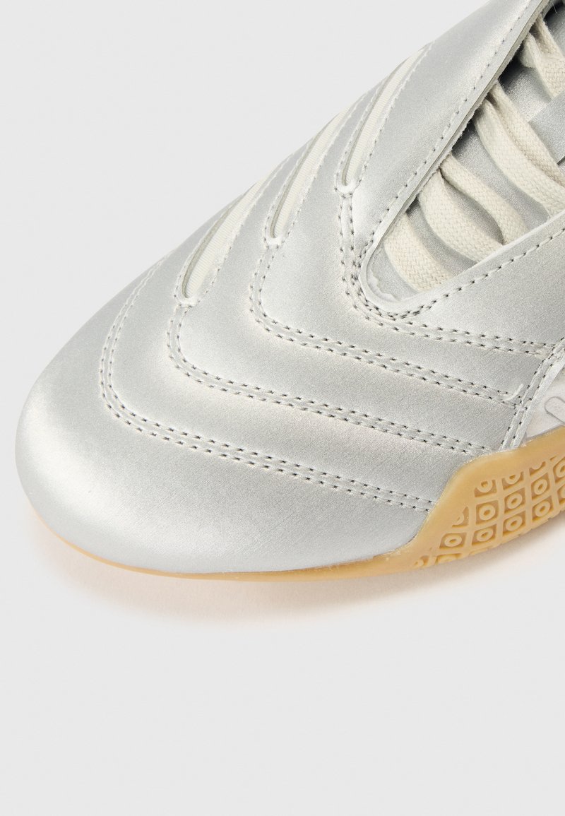 Metallic silver sneaker with textured, stitched upper. Features elasticized lace and gum rubber sole with a square pattern.