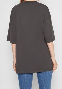 Tmavě šedé oversize tričko s krátkými rukávy a kulatým výstřihem, vyrobené z měkké bavlněné látky, spárované se světle modrými džíny.