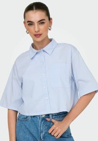 Camisa corta de manga corta en azul claro con rayas verticales blancas, con botones en el frente y un bolsillo en el pecho. Material de mezcla de algodón.