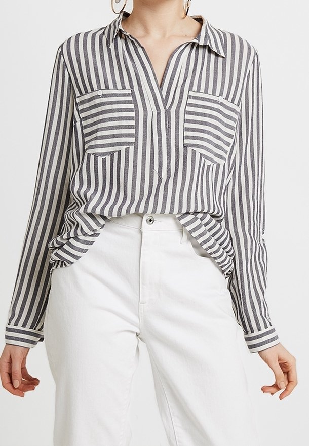 Camicia a maniche lunghe a righe grigie e bianche, con collo, due tasche frontali e vestibilità ampia, abbinata a pantaloni bianchi.