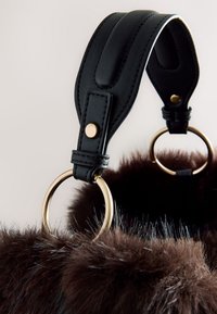Sangle en cuir noir avec des anneaux métalliques dorés fixés à un matériau doux en fourrure brun foncé, probablement une partie d’un sac à main ou d’un accessoire.