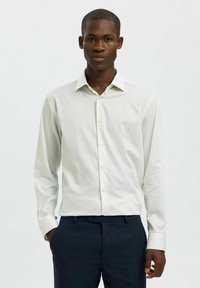 Hellgrünes Langarmhemd mit vertikalen Streifen, Button-Down-Kragen und gelben Knöpfen, kombiniert mit navyfarbener Hose. Glatte Textur.