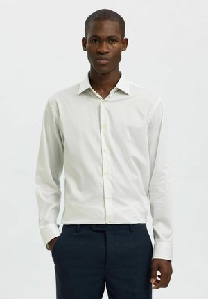 Light green, long-sleeve shirt with vertical stripes, button-down collar, and yellow buttons, worn with navy trousers. Smooth texture.