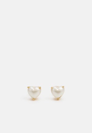 Heart-shaped earrings in pearlescent white, set in gold-tone metal. Smooth texture with visible hardware accents. Each earring features two prongs.