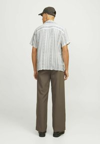 Chemise à manches courtes avec une base blanche et des motifs verticaux bleus, assortie à un pantalon brown ample et des chaussures noires. Différentes caractéristiques de design sont visibles.