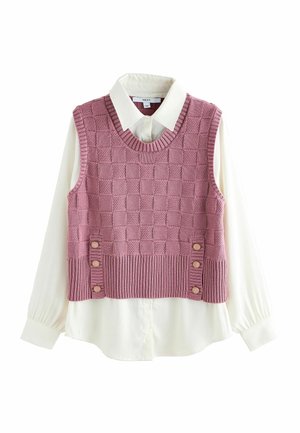 Chemise crème à manches longues avec col sous un gilet sans manches en maille rose à motif à carreaux et boutons décoratifs près de l'ourlet.
