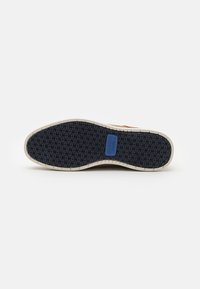Talpa de pantof cu un model texturat din cauciuc negru, marginile bej și un accent cu logo albastru. Proiectată pentru aderență și durabilitate.