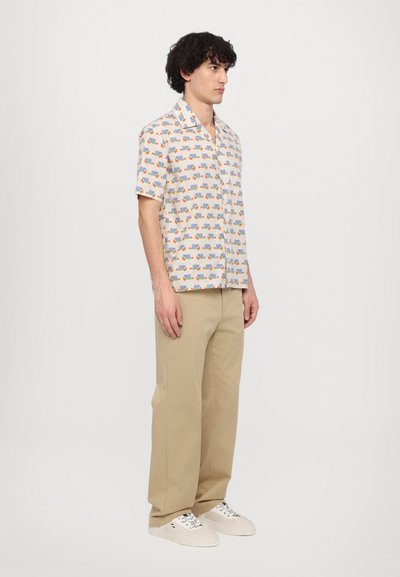 Chemise à manches courtes en tissu crème avec une impression colorée de divers objets. Associée à un pantalon large beige et des baskets légères.