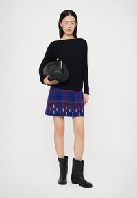Maglione nero di maglia, gonna a quadri blu con accenti rossi e bianchi, e stivaletti neri alla caviglia. Modella con una borsa a tracolla rotonda nera.