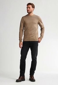 Pulover tricotat maro deschis cu decolteu rotund, asortat cu blugi negri și cizme maro cu șireturi. Textură netedă cu manșete strânse.