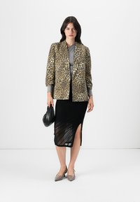 Blazer s uzorkom leoparda, sivi top, crna rebrasta midi suknja s bočnim prorezom, špicaste svijetlosive štikle i mala crna torbica.