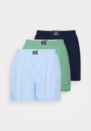 Trois paires de boxers en coton pour hommes, de couleur bleu clair, vert et marine, avec des ceintures élastiques et une étiquette sur chaque paire.