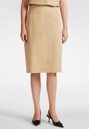 Gonna a tubino beige lungo fino al ginocchio con una superficie liscia, caratterizzata da una silhouette aderente e cuciture laterali, abbinata a décolleté slingback nere con punta a stiletto.