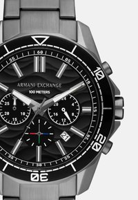 Nerūdijančio plieno chronografas su juodu tekstūruotu ciferblatu, trimis sub-ciferblatais, sidabriniais rodyklėmis ir datos langu. Atsparus vandeniui iki 100 metrų.