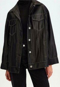 Zwarte satijnen jack met een grote kraag, twee borstzakken en contrasterende witte stiksels. Voorzien van zilveren knopen en een relaxte pasvorm.