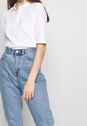 Polo shirt blanc avec un col et des boutons, associé à un jean taille haute bleu clair. Le tissu semble lisse, avec une coupe décontractée.