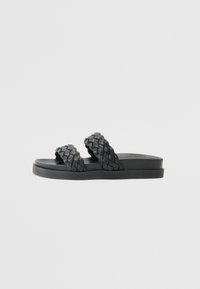 Svarte sandaler har to flettede stropper og en flat, teksturert såle. Designet er minimalistisk med en glatt overflate og uten dekorasjoner.