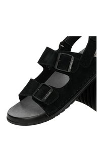 Schwarze Sandale mit offenen Zehen, zwei verstellbaren Riemen mit Schnallen, die mit "wojas" beschriftet sind, weiches graues Fußbett und ein ungewöhnlich geriffelter hoher Absatz.