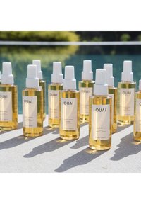 Heldere glazen sprayflacons met witte pompen, gevuld met een licht amberkleurige vloeistof. Etiketten lezen "OUAI Wave Spray", met zwarte tekst en een minimalistisch ontwerp.