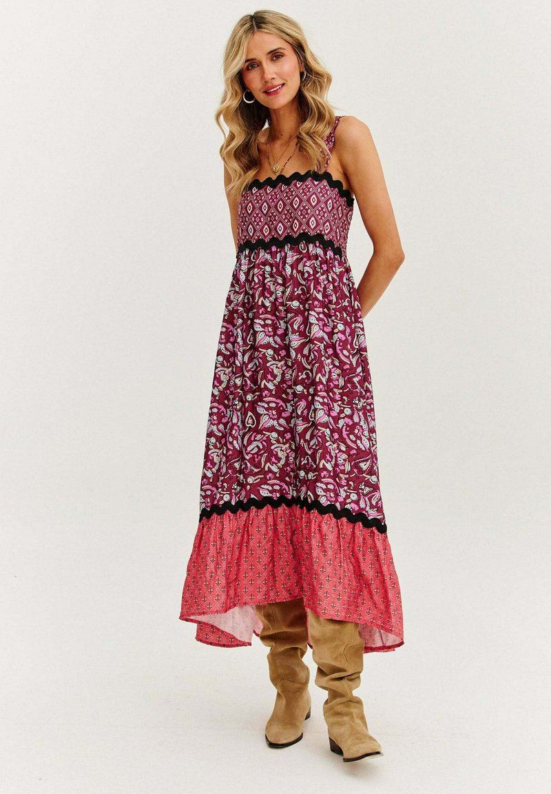 Maxi sukienka w burgundowy kwiatowy wzór, z czarnymi koronkowymi akcentami i różowym wzorem u dołu, wykonana z lekkiej tkaniny. W połączeniu z beżowymi botkami do kolan.