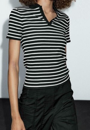 Person wearing a black and white horizontal striped short-sleeve shirt and high-waisted black pants against a plain background.