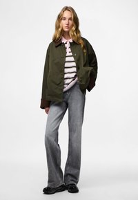 Oliivroheline jakk pruunide aktsentidega, kantud roosa ja triibulise sädaga särgi peale. Heledad hallid laiad teksad ja mustad kingad lõpetavad komplekti.