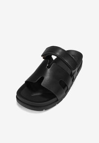 Black sandals featuring a slip-on design with two wide straps, made of smooth material. The sole is thick and textured for grip.