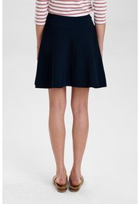 Rok berflare navy dengan tekstur halus, sepanjang lutut. Dipadukan dengan sandal coklat muda, dikenakan dengan atasan lengan panjang bergaris merah muda dan putih.