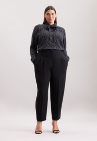 Zwarte blouse met polka dots en een strikhalslijn, gecombineerd met zwarte high-waisted broek met zijzakken en een gladde textuur.