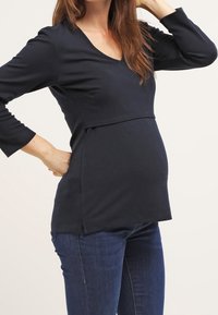 Těhotenský top s dlouhým rukávem v námořnické modré barvě, s výstřihem do V, vrstveným designem a zakřiveným lemem, který vyhovuje rostoucímu břichu. Jemný textilní materiál.