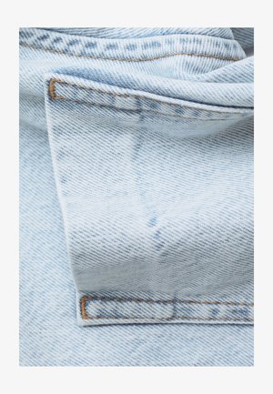 Helles blaues Denimgewebe mit einer weichen Textur, das sichtbare Nähte in einer kontrastierenden braunen Farbe und gefaltete Kanten aufweist.