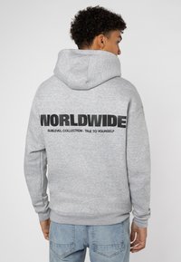 Grijze hoodie met een grote zwarte print op de achterkant met de tekst "WORLDWIDE" en kleinere tekst eronder. Bevat een buidelzak en ribgebreide manchetten.