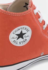 Sapatilha de cano alto laranja em tela com atacadores brancos, apresentando um patch de logótipo de estrela preta e sola de borracha preta com detalhe branco.