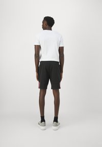 Pantaloni corti da allenamento neri con strisce rosa laterali, abbinati a una t-shirt bianca aderente e sneakers grigie, con una texture semplice.