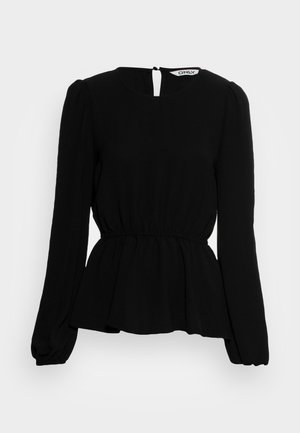 Blouse noire à manches longues avec taille élastique, encolure ronde, légère basque et fermeture avec bouton et ouverture en forme de goutte d'eau dans le dos sous le col.