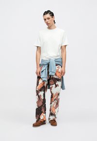 Fehér, kerek nyakú póló, laza fazonú, mintás nadrág lókkal díszítve barna és krémszínben, derékon megkötött világoskék pulóverrel. 