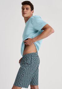 Lichtblauw kortom, gecombineerd met een patroon zwembroek met een geometrisch ontwerp in teal en zwart, elastische tailleband.