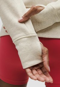 Kremasta majica dugih rukava s rebrastim manžetama, uparena s crvenim uskim šortsevima, koja prikazuje mekanu tkaninu i opušteni kroj.