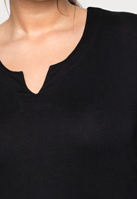 Czarny t-shirt z dekoltem w serek, wykonany z miękkiej, elastycznej tkaniny o gładkiej fakturze. Zauważalny centralny szew przy dekolcie.